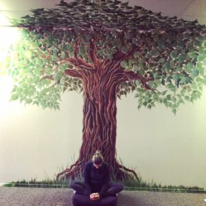 Shannon Renee at yoga sitting under a tree on drawn on the wall in meditation.